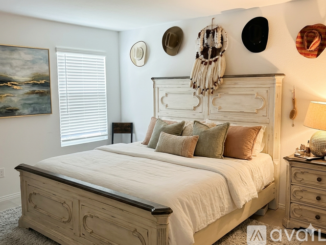A bedroom with a large bed, a painting on the wall, and a window with blinds.
