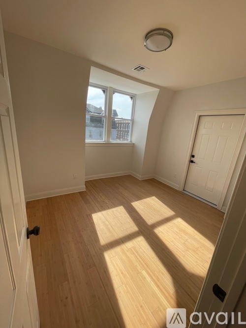 A room with wooden floors and white walls, with a window letting in natural light.