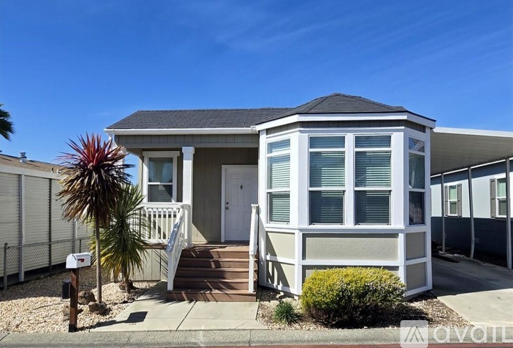 A house with a grey roof and white walls is surrounded by a white fence.