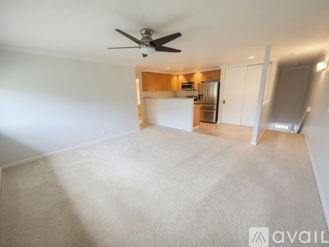 A spacious room with a ceiling fan and a kitchenette in the background.