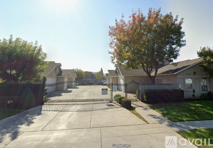 A sunny day in a quiet residential street with houses on both sides and a tree with orange leaves in the foreground.