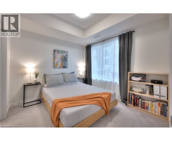 A bedroom with a bed, a nightstand with a lamp, a bookshelf with books, and a painting on the wall.