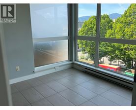 A room with a large window overlooking a street with trees and buildings.