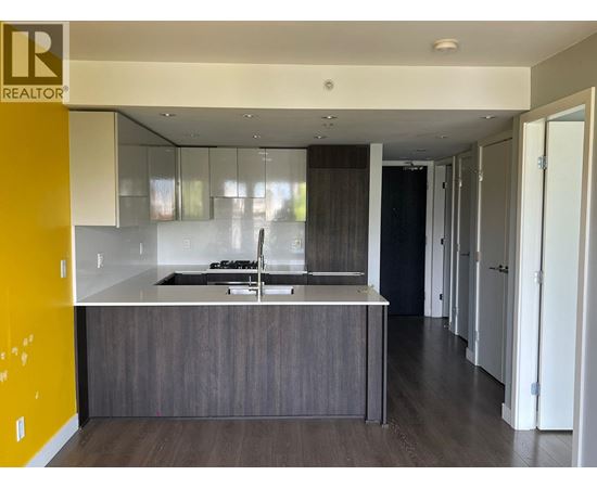 A modern kitchen with a dark wood floor and a yellow accent wall.