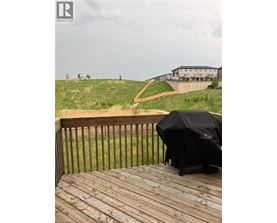 A grill is on a wooden deck overlooking a grassy hill.