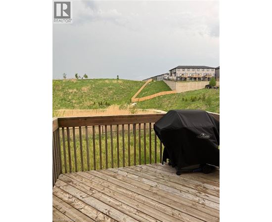 A grill is on a wooden deck overlooking a grassy hill.