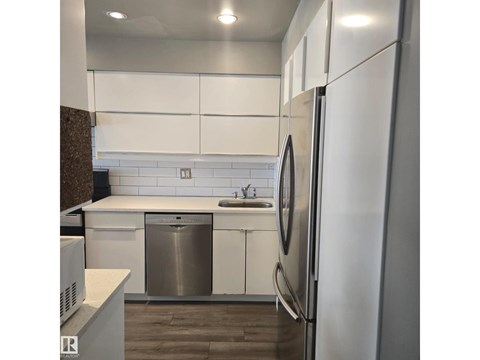 A modern kitchen with white cabinets and a stainless steel dishwasher and refrigerator.