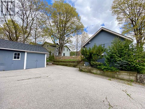 A gravel driveway leads to a garage with a blue house in the background.