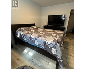 A bedroom with a bed, a television, and a wooden floor.