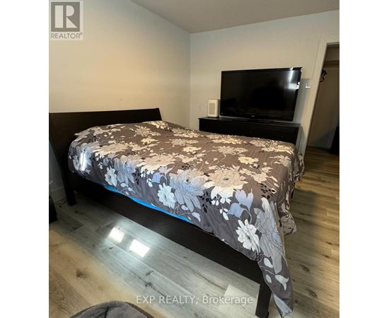 A bedroom with a bed, a television, and a wooden floor.