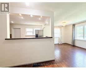 A spacious room with wooden floors and white walls, with a bar area in the corner.