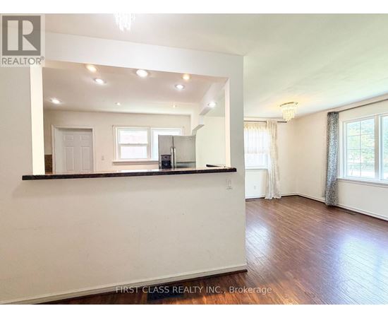 A spacious room with wooden floors and white walls, with a bar area in the corner.