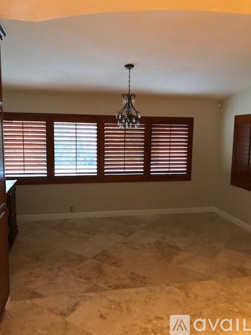 A room with a chandelier, tiled floor, and a window with blinds.
