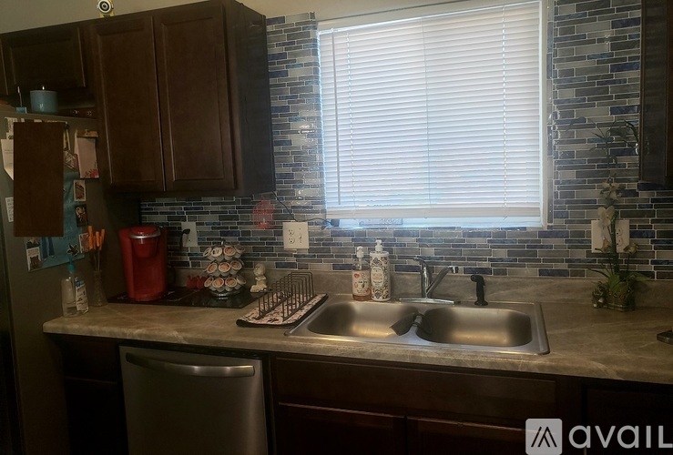 A kitchen with a sink, a window with blinds, and a trash can.