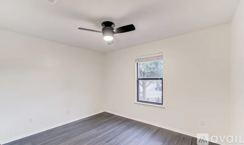 A room with a ceiling fan and a window showing trees outside.