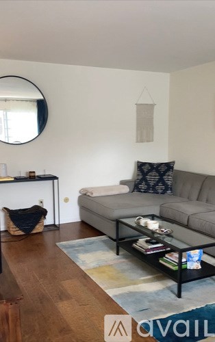 A living room with a grey couch and a round mirror on the wall.