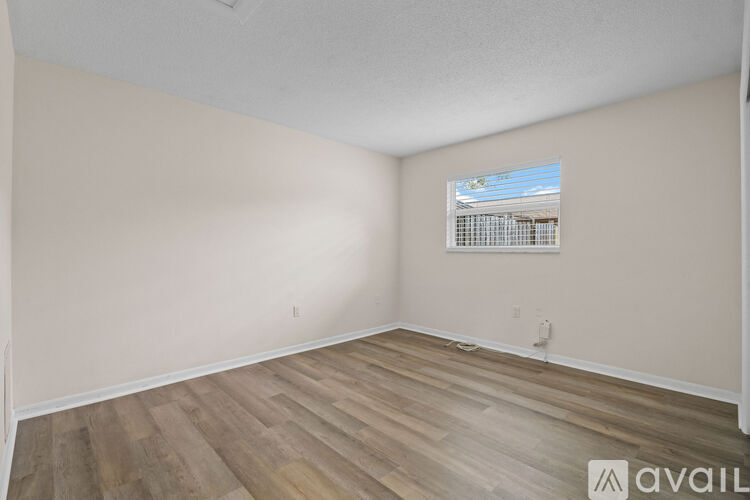A room with wooden flooring and a window showing a view of a building.