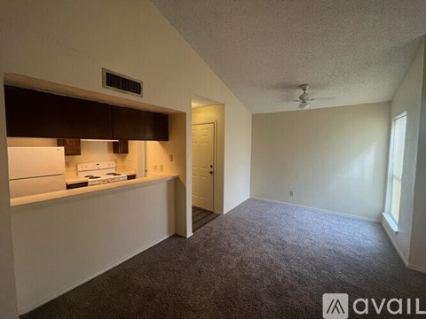 A carpeted room with a small kitchenette and a door leading to another room.