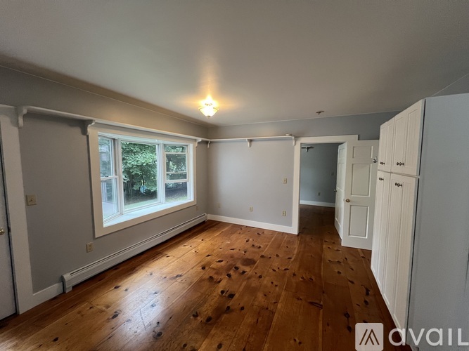 A room with wooden floors and white walls, with a window and a door visible.