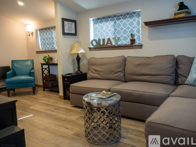 A living room with a grey couch, a blue chair, and a table with a lamp on it.