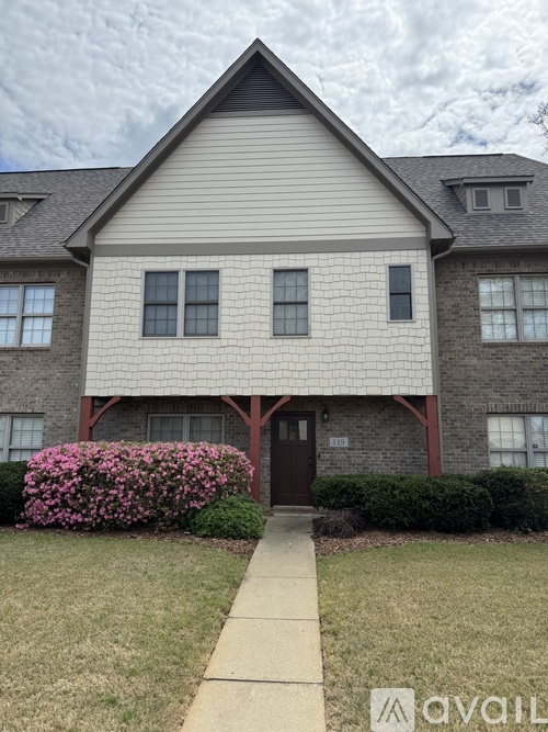 A house with a brown door and windows with a bush in front.