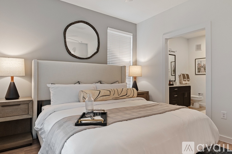 A well-lit bedroom with a large bed, a round mirror, and a nightstand with a lamp.