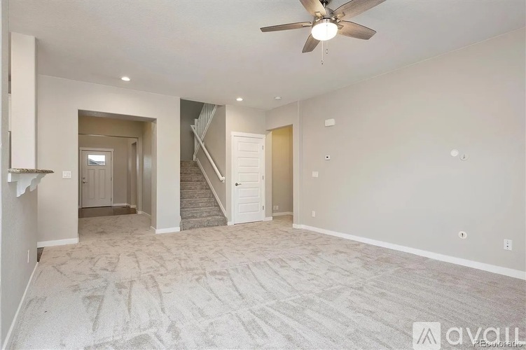 A spacious room with a fan and a staircase in the background.
