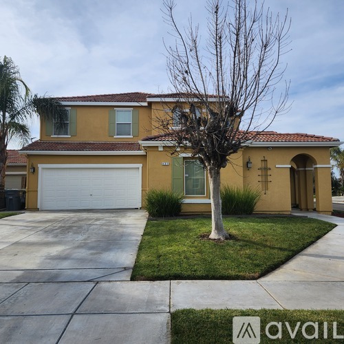 A yellow house with a white garage door and a tree in front.