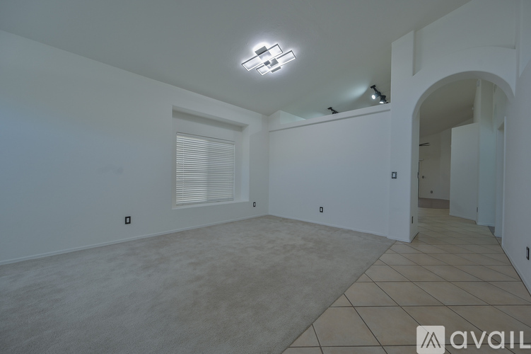 A spacious empty room with a tiled floor and a large archway leading to another room.
