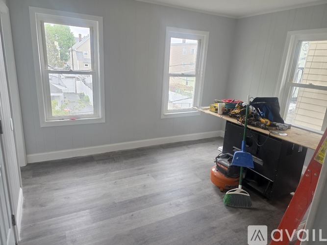 A room with grey flooring and two windows, one of which has a view of a street.