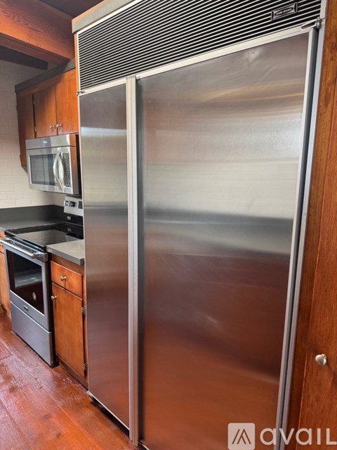 A stainless steel refrigerator stands in a kitchen with wooden cabinets.