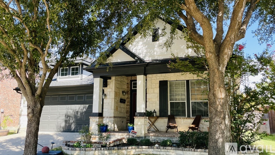 A house with a white exterior and a black roof is surrounded by trees.