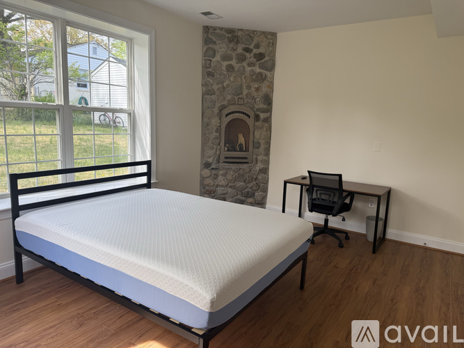 A bedroom with a bed, desk, and a stone fireplace.