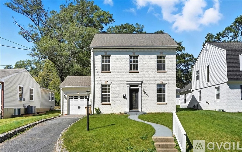A white house with a grey roof is surrounded by a white fence and green grass.