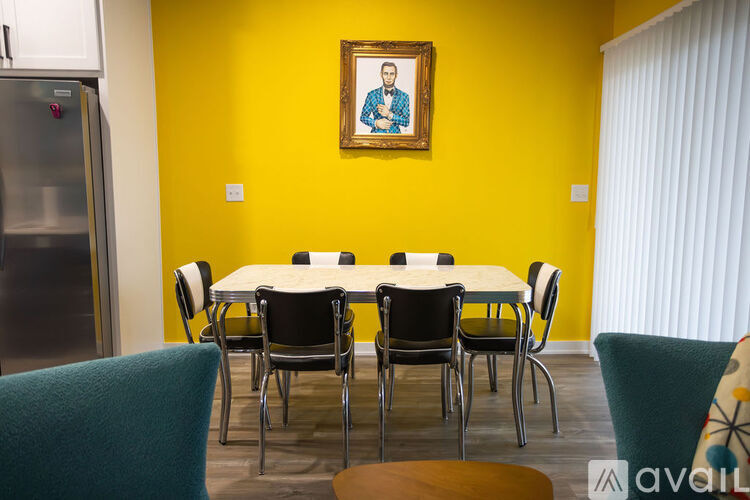 A dining room with a yellow wall and a framed picture hanging above the table.
