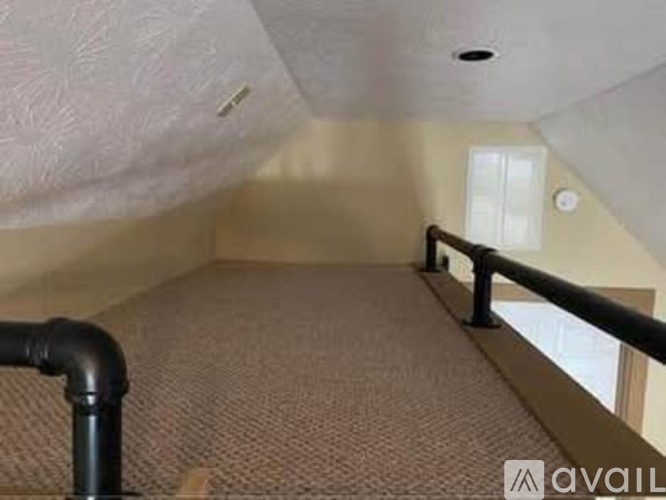 A room with a carpeted floor and a black pipe running along the wall.