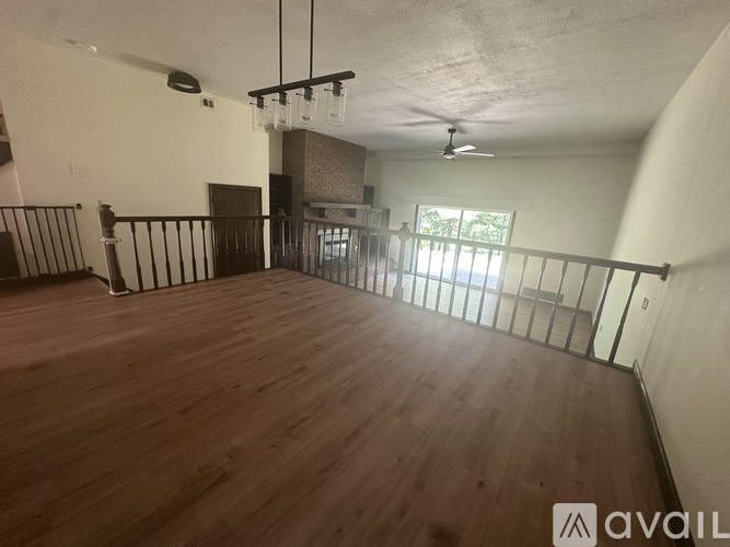 A spacious room with wooden flooring and a balcony with a railing.