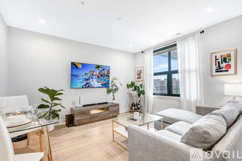 A modern living room with a grey sofa, a glass table, and a painting on the wall.