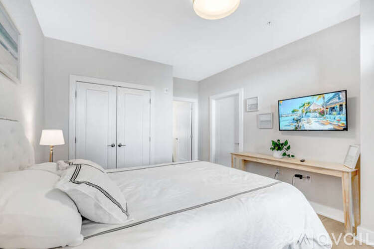 A bedroom with a bed, a desk with a plant, and a painting on the wall.