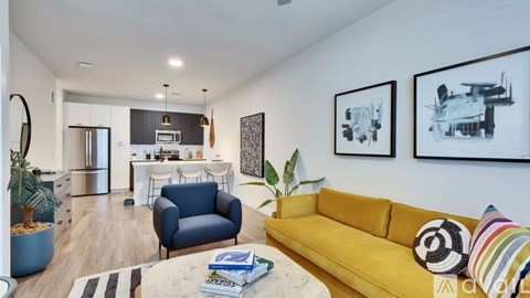 A living room with a yellow couch and a dining area in the background.