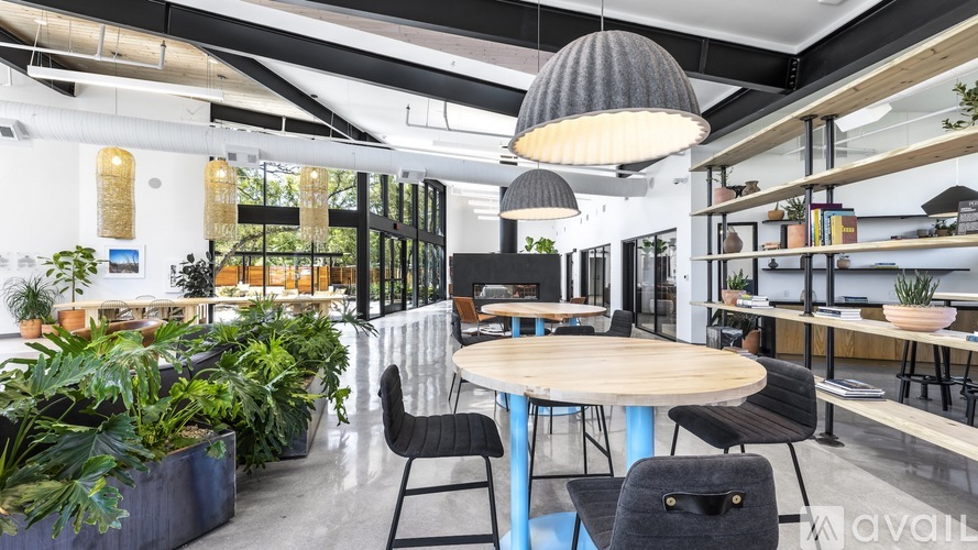 A modern office space with a round table and chairs, surrounded by plants and shelves with books and decorations.