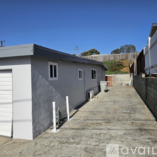 A grey building with a white door and windows is surrounded by a concrete ground.