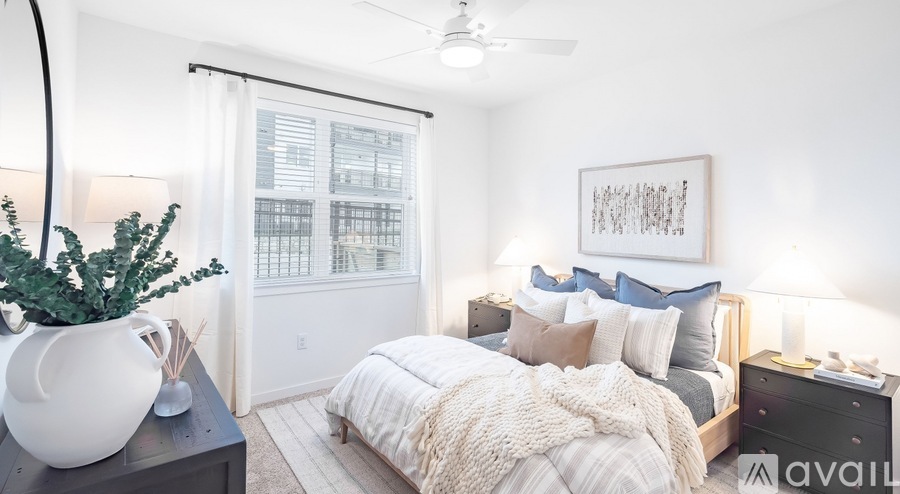 A bedroom with a large bed, a ceiling fan, and a plant on a table.