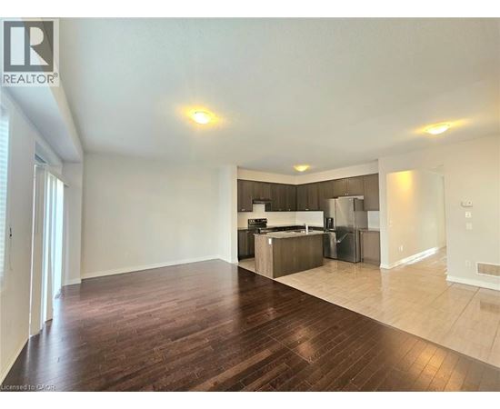 A spacious living room with hardwood floors and a kitchen in the background.