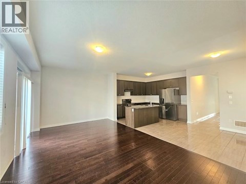A spacious living room with hardwood floors and a kitchen in the background.