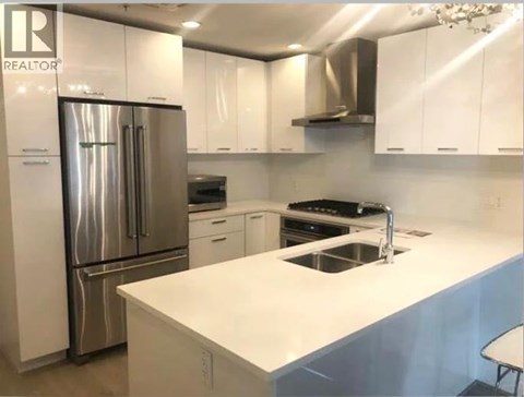 A white kitchen with a stainless steel refrigerator and a white countertop.