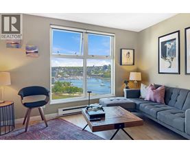 A living room with a grey couch, a black chair, a wooden coffee table, and a large window with a view of the city.