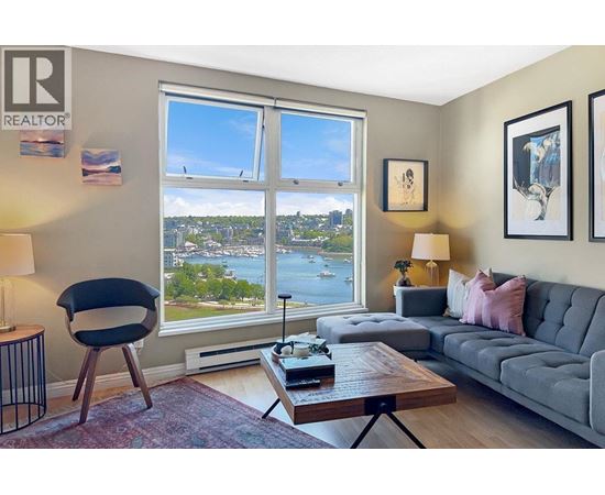 A living room with a grey couch, a black chair, a wooden coffee table, and a large window with a view of the city.