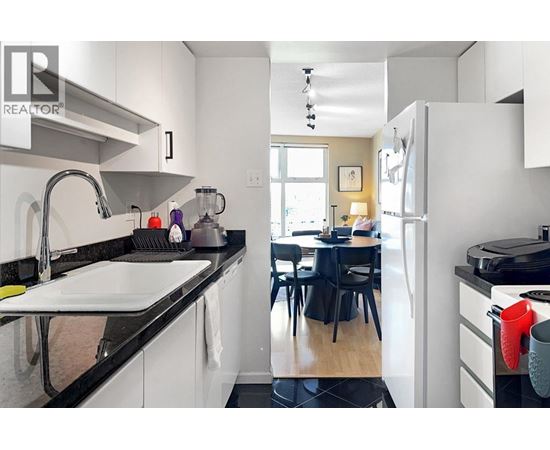 A kitchen with a sink, refrigerator, and a dining table with chairs.