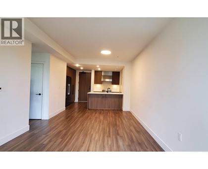A spacious room with wooden floors and a kitchenette in the background.